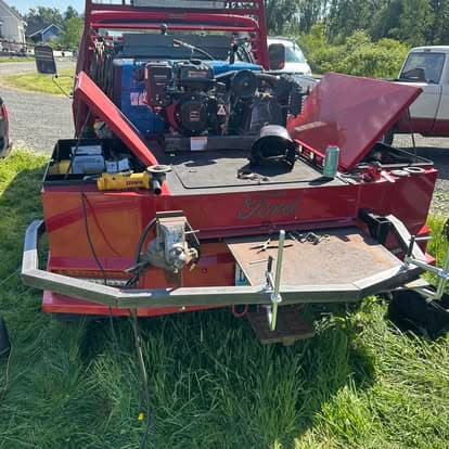 Red Ford truck with open back, showcasing engines and tools on grass.