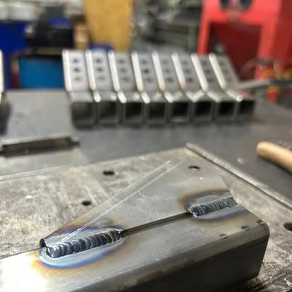 Metal welding process with detailed bead on a steel workpiece in a workshop setting.