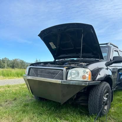 Black SUV with hood open, parked on a grassy roadside under a clear blue sky.