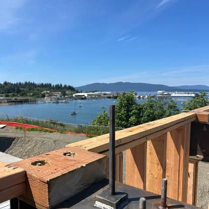 View of a harbor with boats, mountains, and clear blue sky from a construction site.