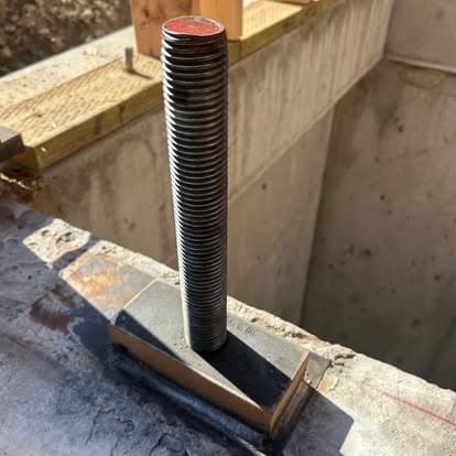 Steel anchor bolt installed in concrete foundation with threads visible.