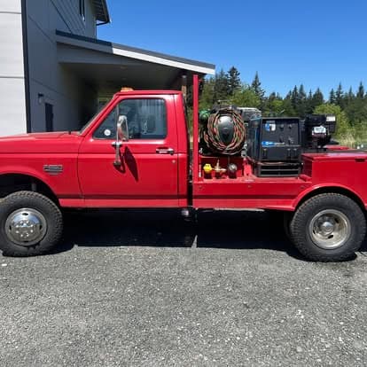 Red pickup truck with equipment in the bed, parked outside a building in a clear blue sky.