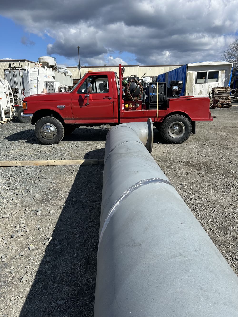 Red pickup truck parked next to a large pipe at a construction site under cloudy skies.