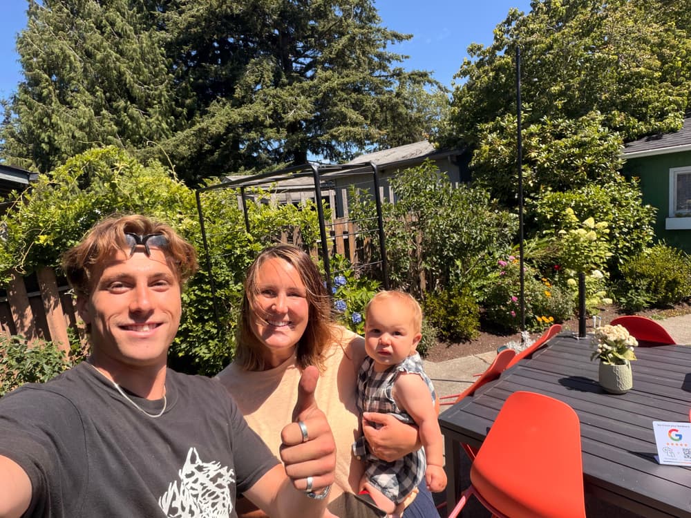 Happy family selfie in a sunny backyard garden, featuring a parent and toddler.