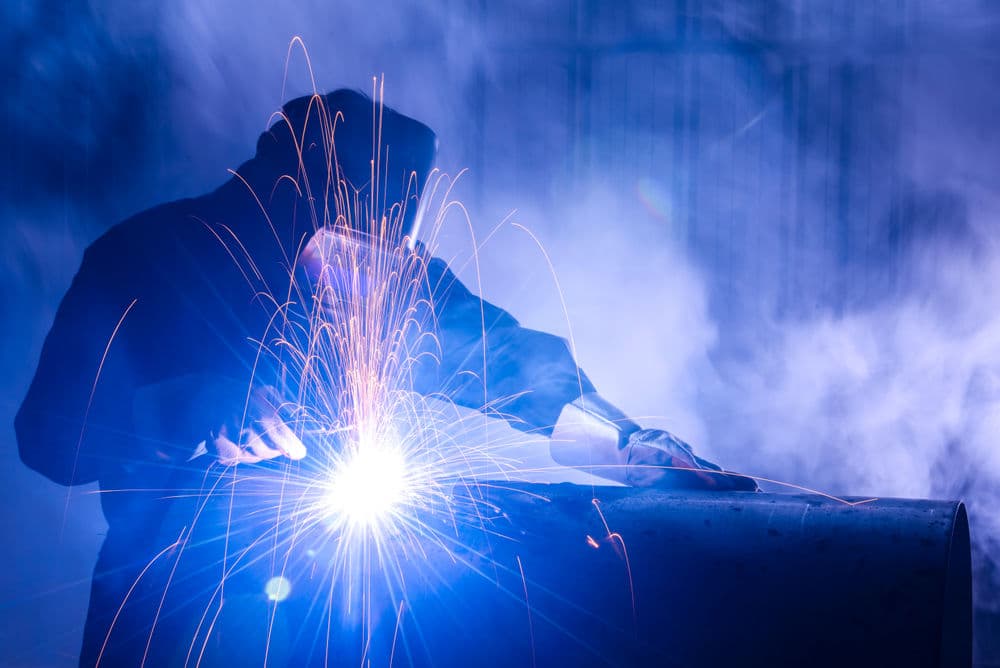 Worker welding metal with vibrant sparks in a smoky, blue-lit environment.